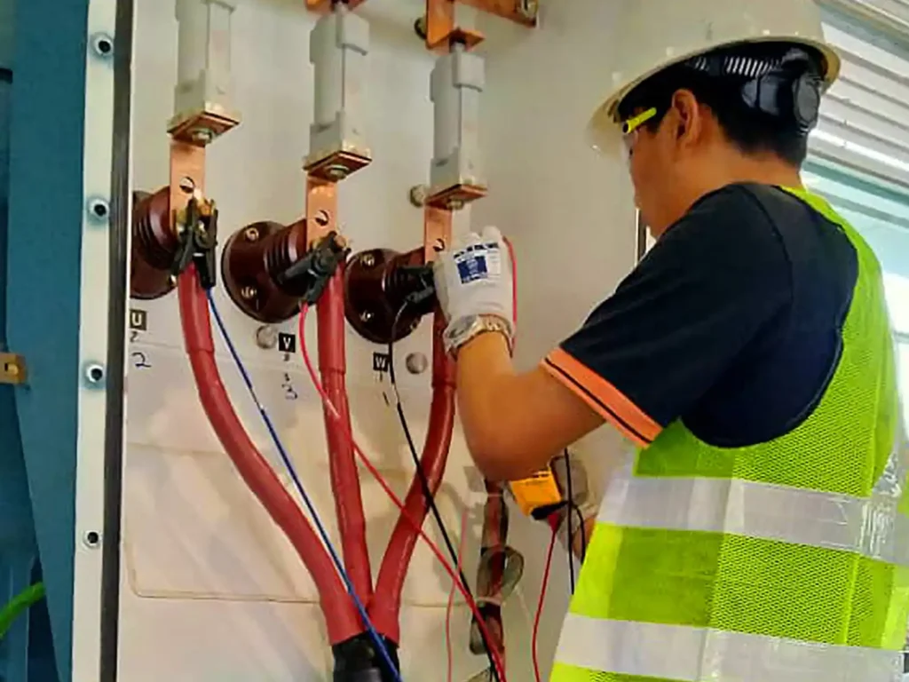 Technician connecting test leads to three-phase motor cables inside an electrical control panel for motor electrical diagnostics