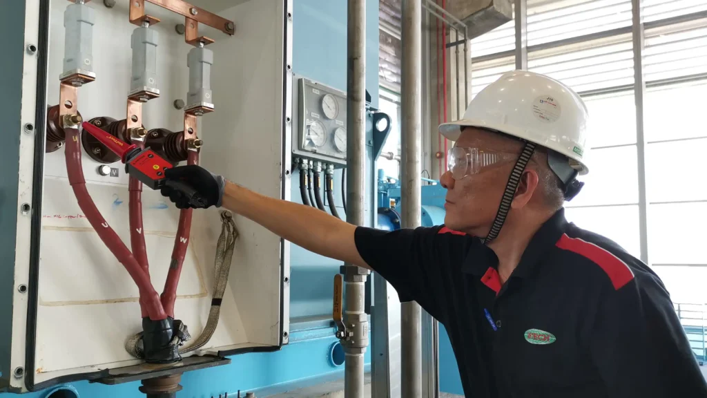 A technician uses a handheld motor-testing device to take electrical measurements from three-phase cables inside a motor control panel.
