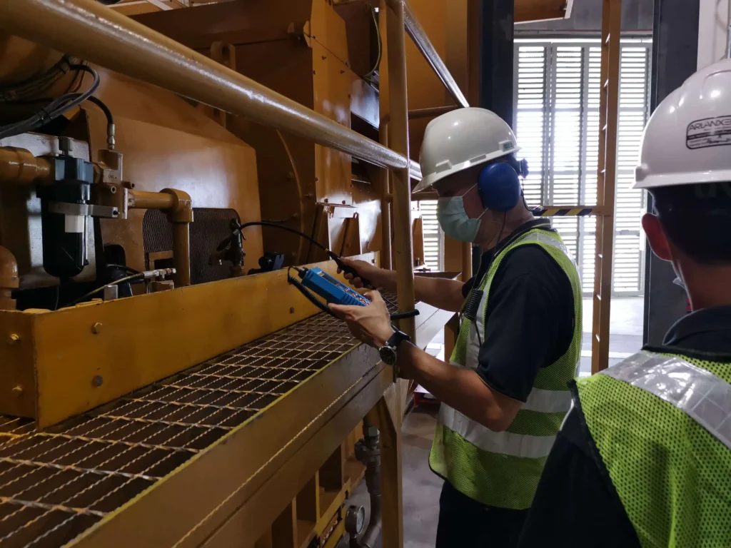 Technician inspecting industrial compressed air equipment for leaks using a handheld ultrasound detector