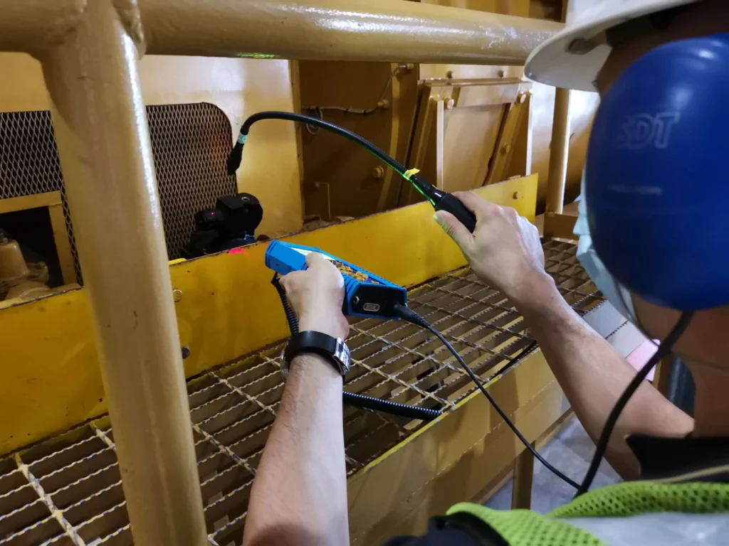 Technician performing an airborne ultrasound inspection of industrial machinery with a handheld detector.