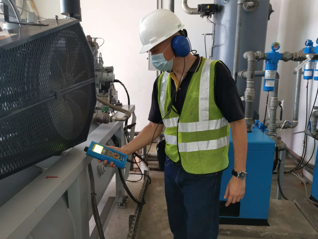 Technician performing compressed air leak detection with an ultrasound detector in an industrial facility