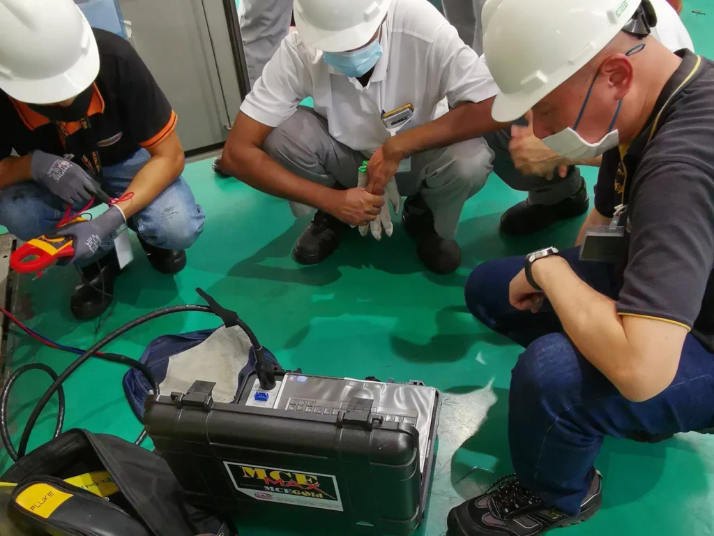 Technicians setting up motor current signature analysis equipment and measuring electrical current during an industrial motor inspection.