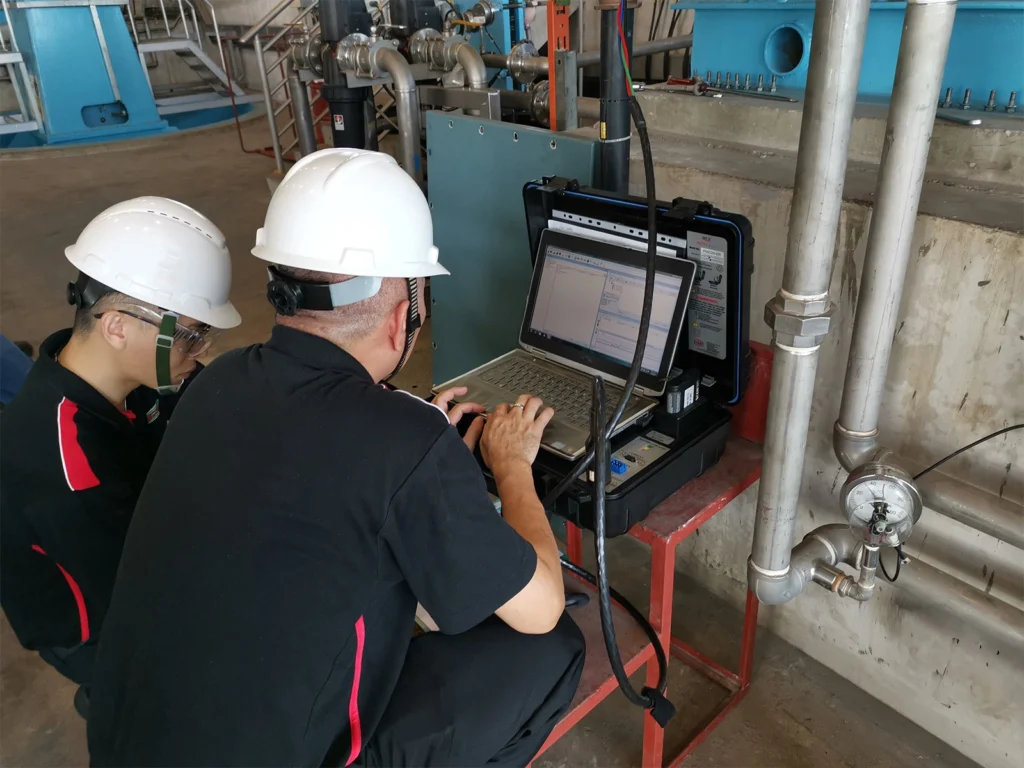 Two technicians reviewing motor diagnostic data on a laptop connected to portable electrical testing equipment at an industrial pump system