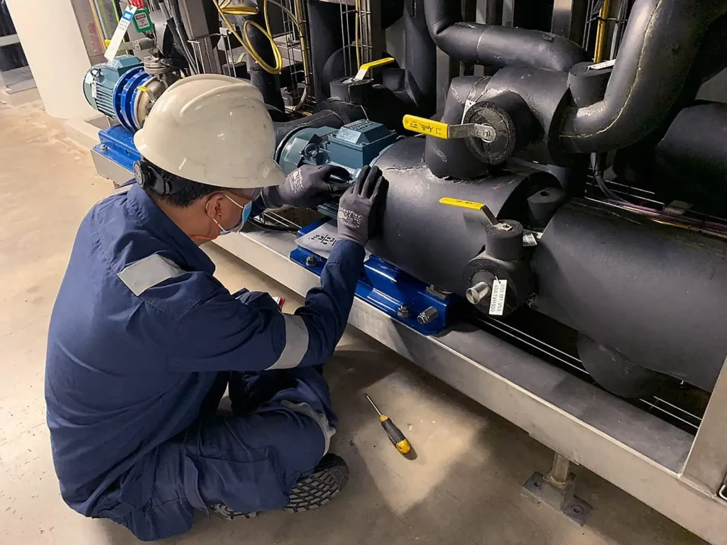 Technician inspecting an industrial pump and pipework assembly in a mechanical plant room.